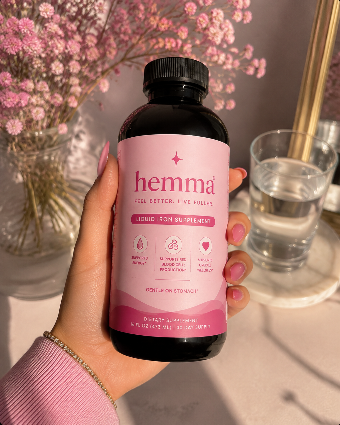 Hand holding hemma liquid iron supplement in sunlight beside pink flowers